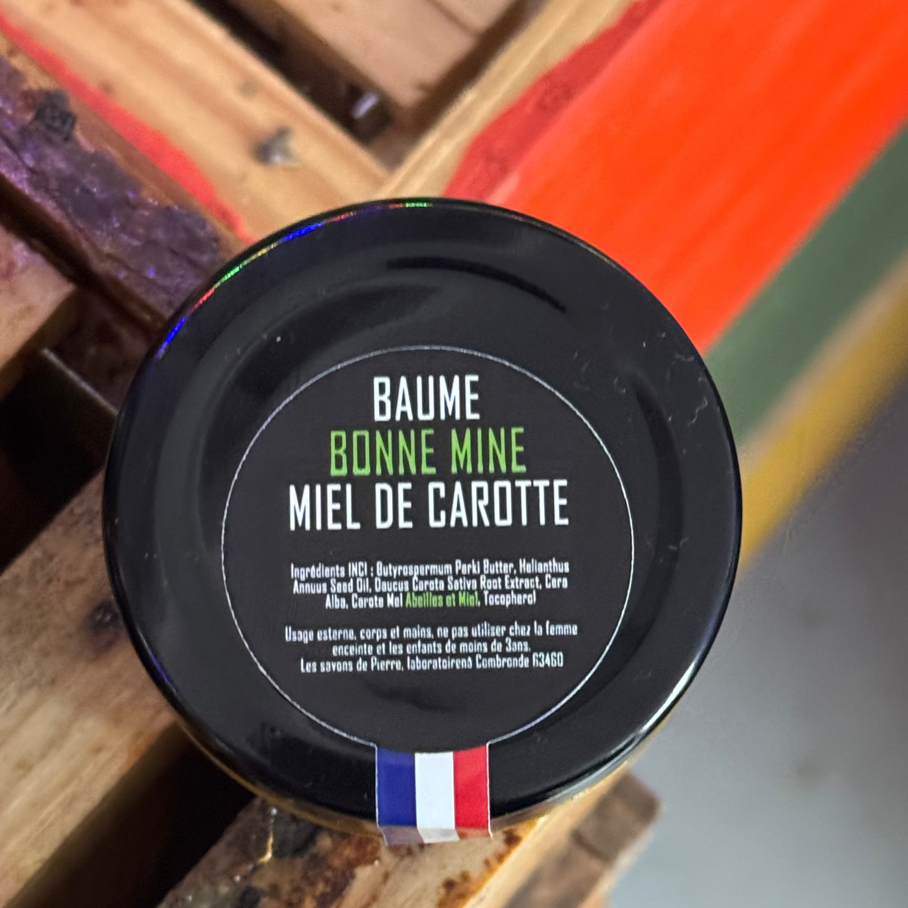 Pot de baume visage au miel de carotte et extrait de carotte, présenté dans un univers chaleureux illustrant son effet bonne mine et sa texture riche.