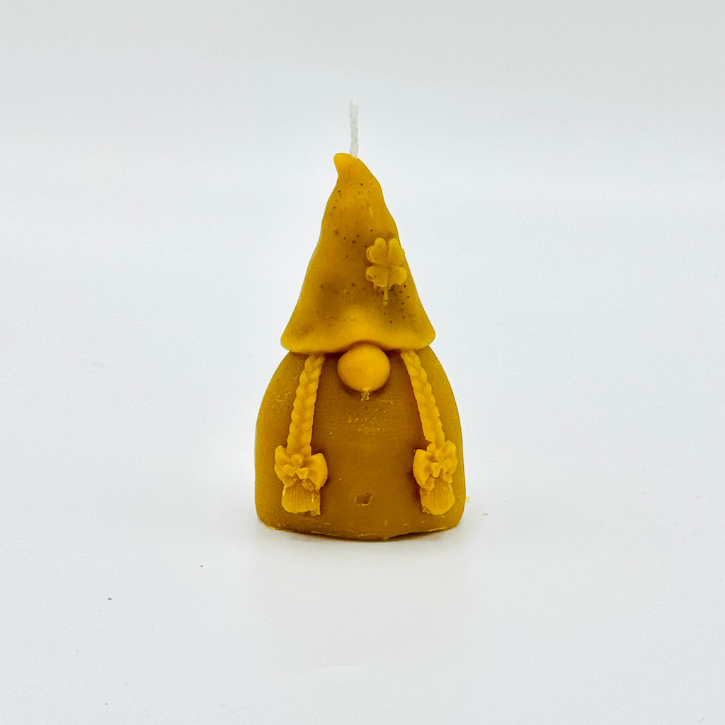 Bougie artisanale en cire d’abeille représentant un lutin avec bonnet pointu, tresses et fleurs sculptées.